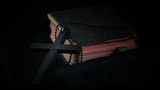 Black Cross leaning on Black Hardcover Bible