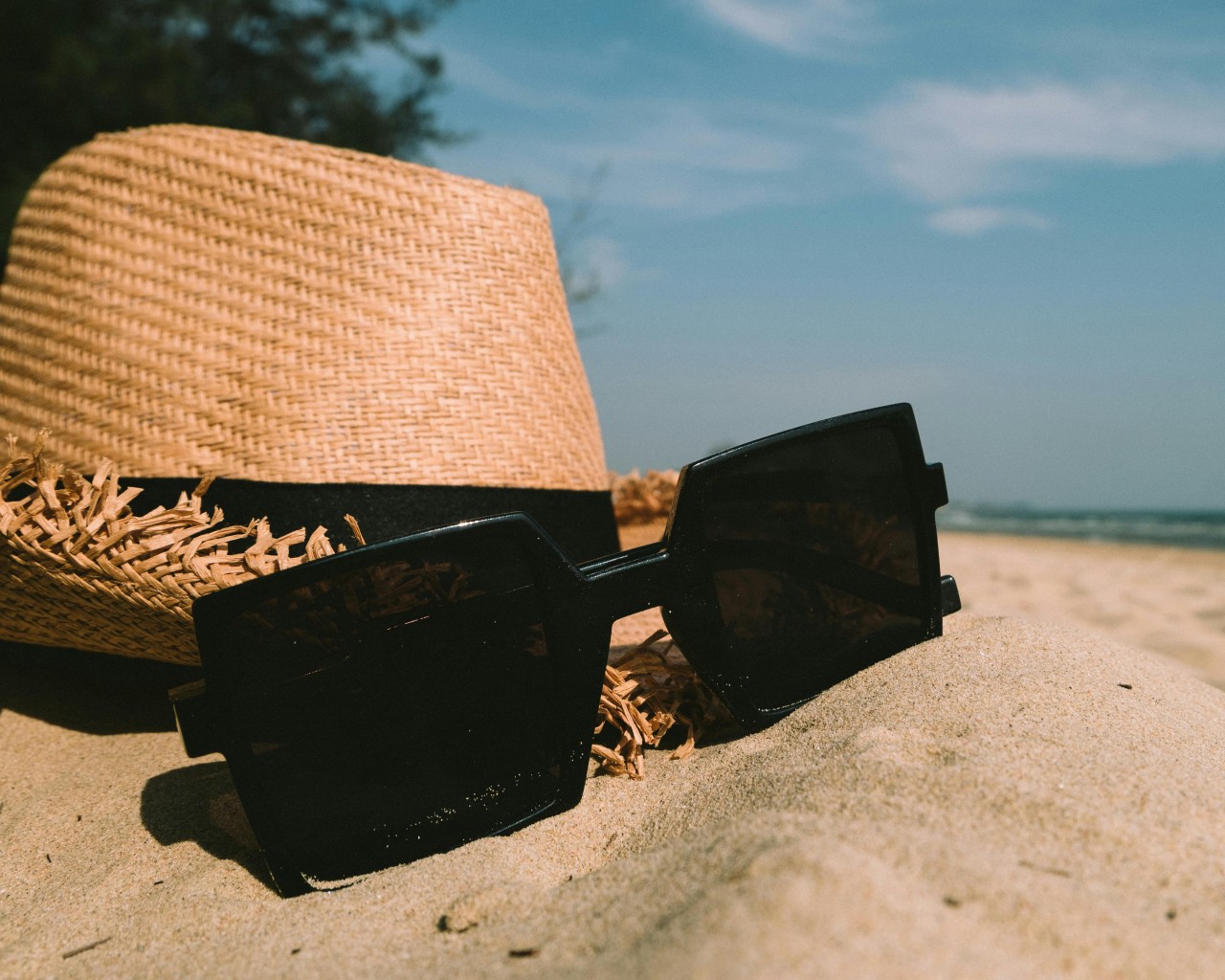 Sunglasses Beside Sun Hat on Sand