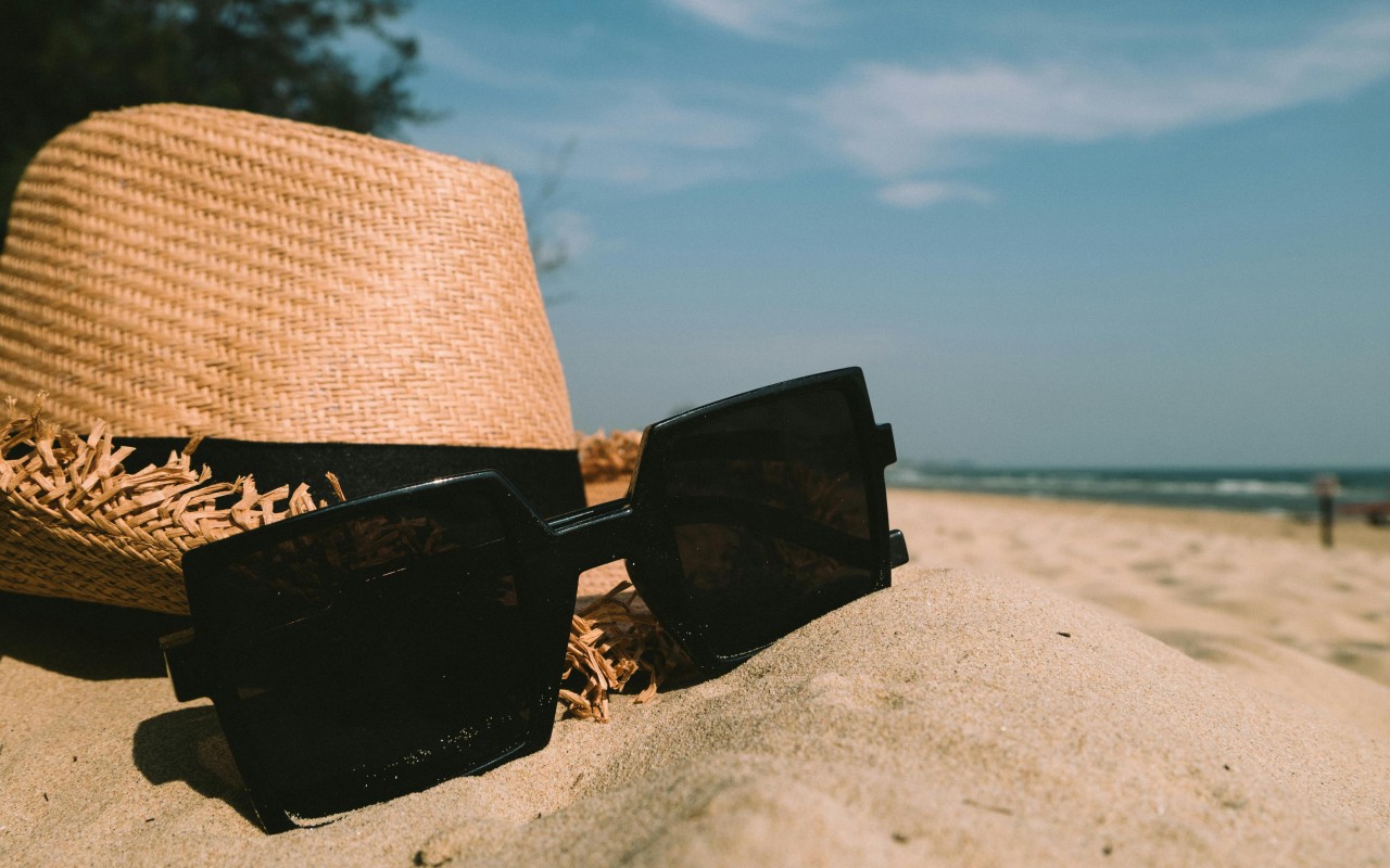 Sunglasses Beside Sun Hat on Sand