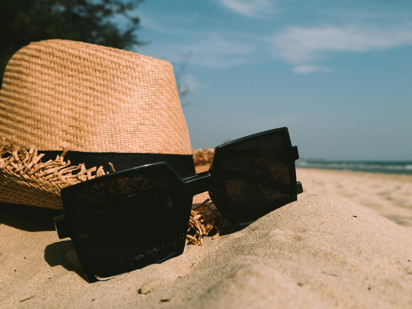Sunglasses Beside Sun Hat on Sand