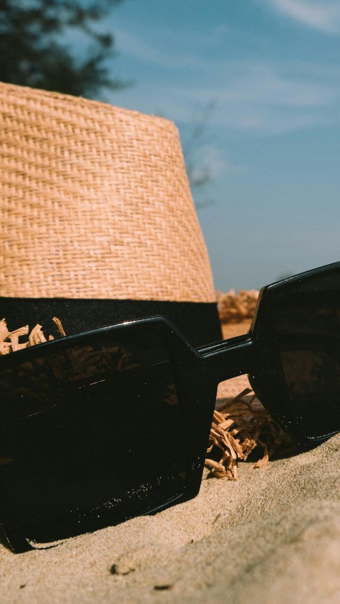 Sunglasses Beside Sun Hat on Sand