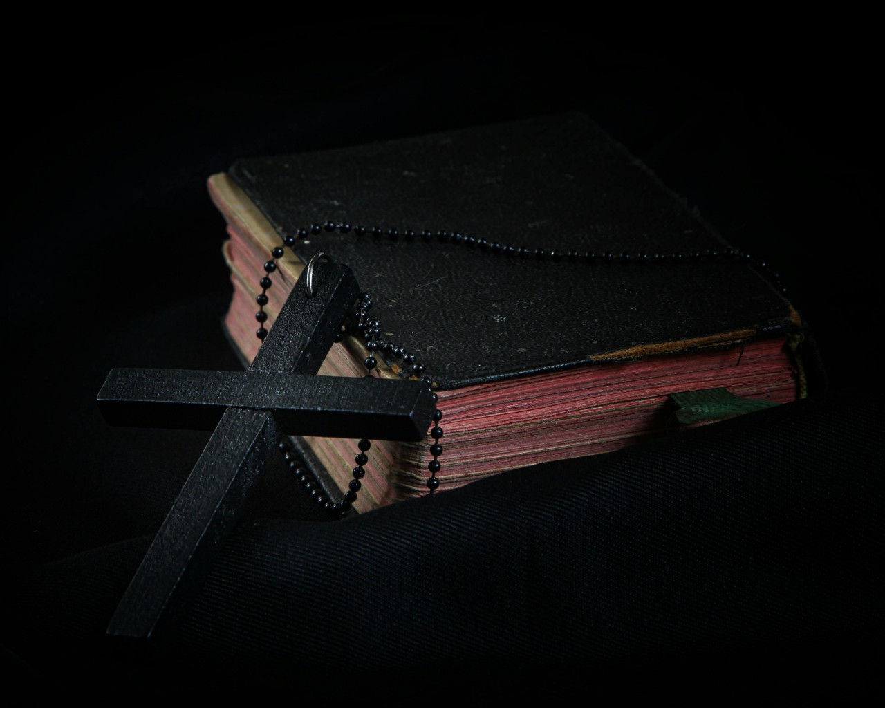 Black Cross leaning on Black Hardcover Bible