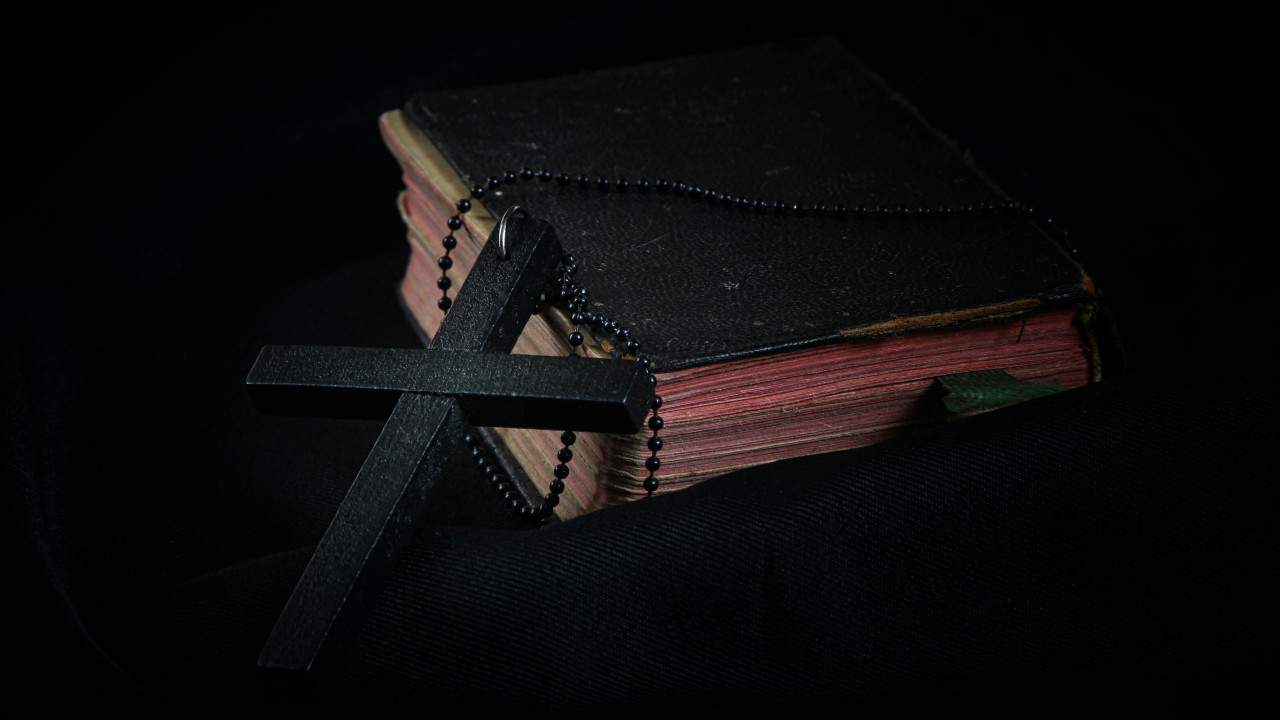Black Cross leaning on Black Hardcover Bible