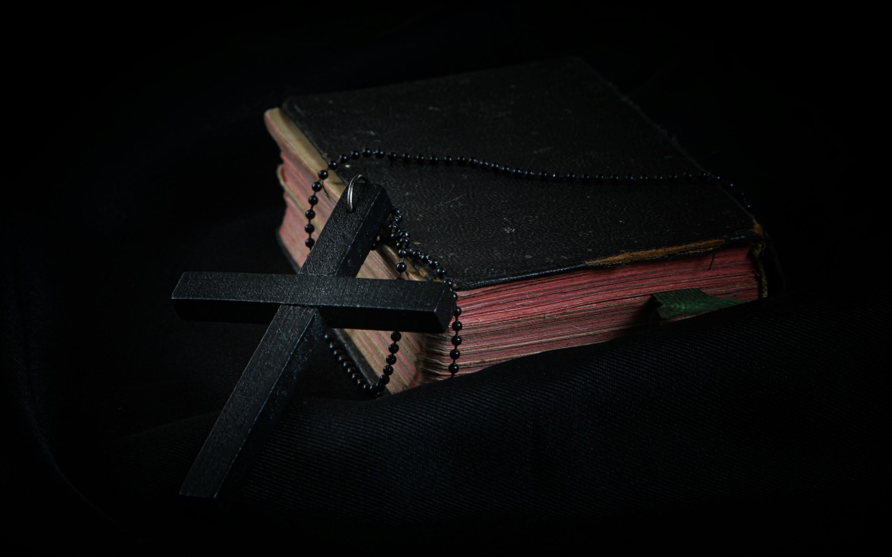 Black Cross leaning on Black Hardcover Bible