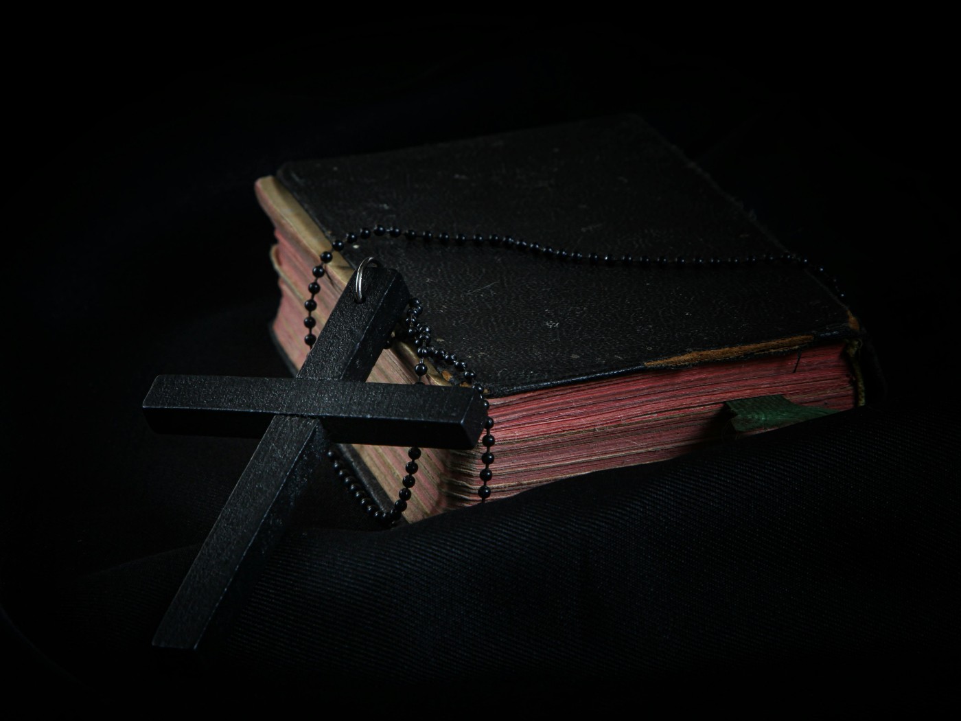 Black Cross leaning on Black Hardcover Bible