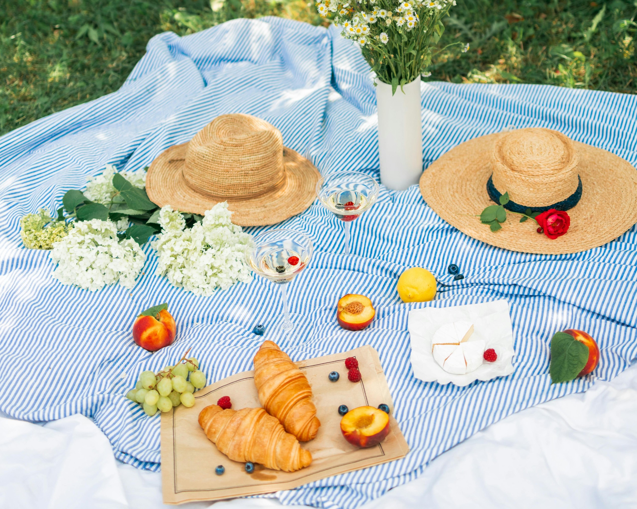 Food Beside the Flowers and Straw Hats on a Picnic Blanket