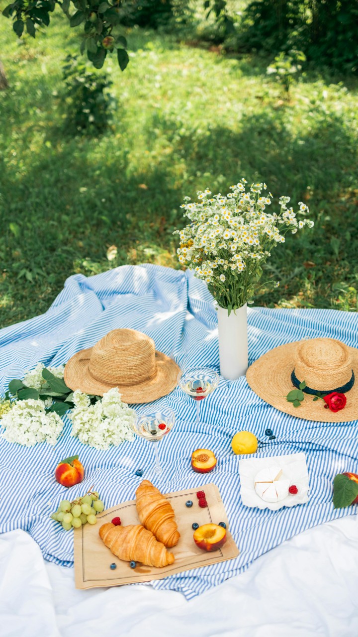 Food Beside the Flowers and Straw Hats on a Picnic Blanket