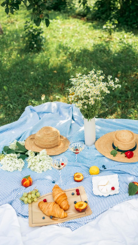 Food Beside the Flowers and Straw Hats on a Picnic Blanket